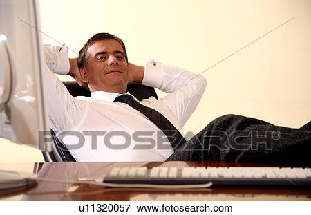Businessman sitting at his desk with hands behind his head View Large Photo Image Stock Photo - Businessman sitting at his desk with hands behind his head. Fotosearch