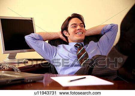 Stock Image - Young businessman relaxing with hands behind head. Fotosearch