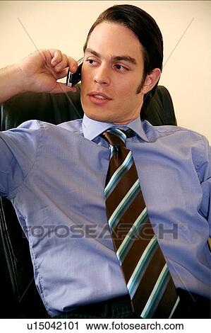 Stock Image - Young businessman sitting and talking on cell phone. Fotosearch