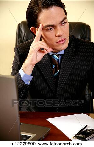 Young businessman sitting at desk and thinking View Large Photo Image Stock Image - Young businessman sitting at desk and thinking . Fotosearch