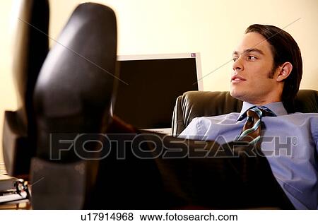 Stock Photo - Young businessman sitting with feet on desk. Fotosearch