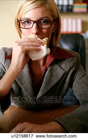 Young woman eating at her desk View Large Photo Image Stock Photo - Young woman eating at her desk. Fotosearch