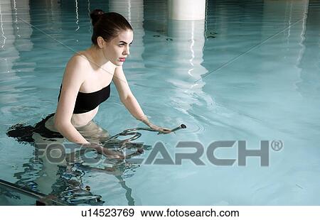 Stock Photo - Young woman on exercise bike in spa pool. Fotosearch