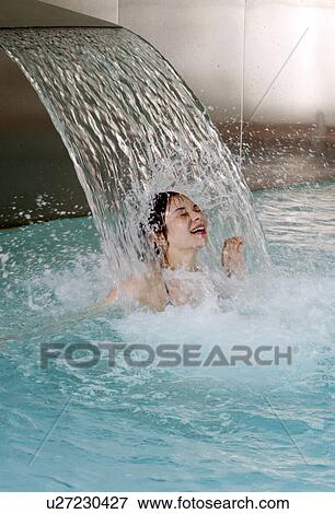 Stock Photo - Young woman standing under water spray in spa pool. Fotosearch
