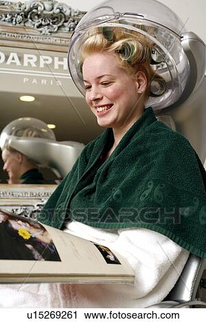Stock Image - Young woman sitting under hairdryer. Fotosearch