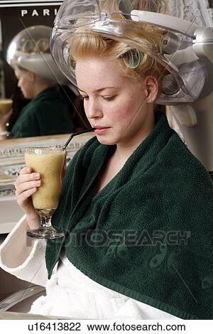Stock Image - Young woman sitting under hairdryer. Fotosearch