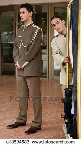 Bellboy Delivering Luggage To Hotel With Doorman Standing By Stock
