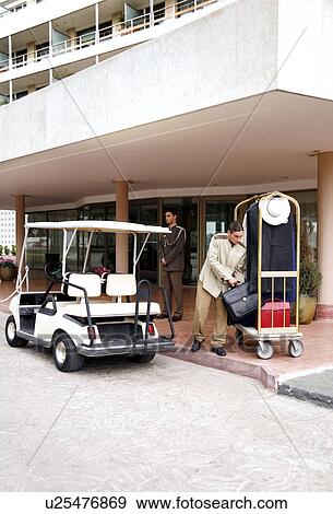 Stock Photo - Bellboy delivering luggage to hotel with doorman standing by. Fotosearch