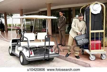 Stock Photograph - Bellboy delivering luggage to hotel with doorman standing by. Fotosearch