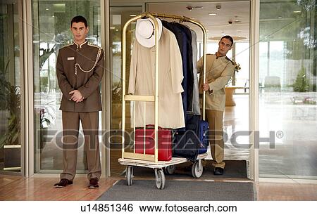 Stock Photograph - Bellboy delivering luggage to hotel with doorman standing by. Fotosearch