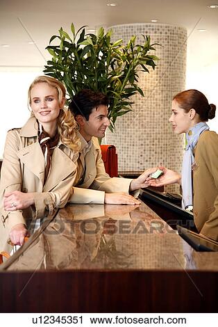 Stock Image - Couple checking in at hotel reception. Fotosearch