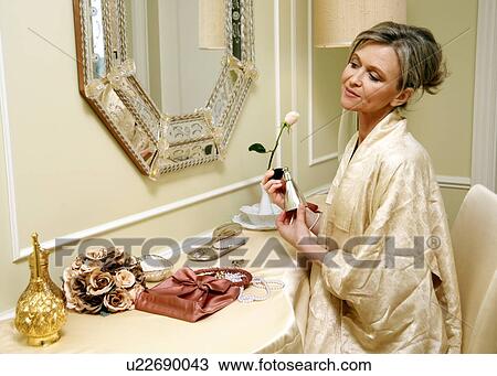 Stock Image - Woman sitting at the dressing table and spraying perfume . Fotosearch