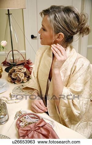 Woman sitting at the dressing table and putting in ear ring View Large Photo Image Stock Image - Woman sitting at the dressing table and putting in ear ring. Fotosearch