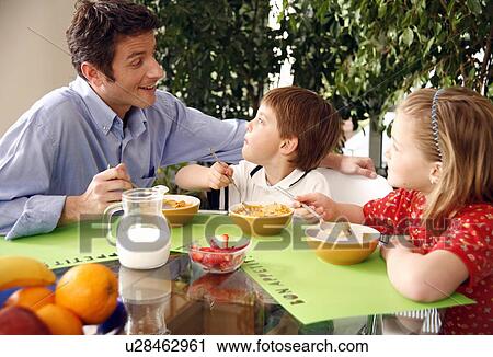 Stock Image - Father and children eating breakfast. Fotosearch