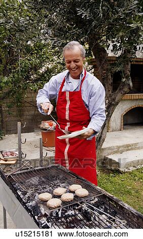 Stock Image - Mature man cooking food at a barbecue. Fotosearch