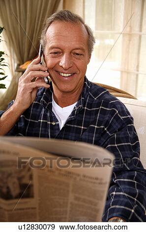 Mature man reading newspaper and talking on cell phone View Large Photo Image Stock Photo - Mature man reading newspaper and talking on cell phone. Fotosearch