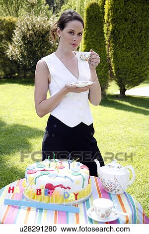 Stock Image - Woman with Birthday cake, teapot and cups. Fotosearch