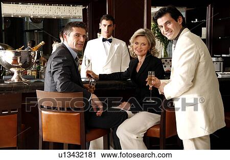 Stock Image - Two men and a woman sitting at a bar drinking. Fotosearch