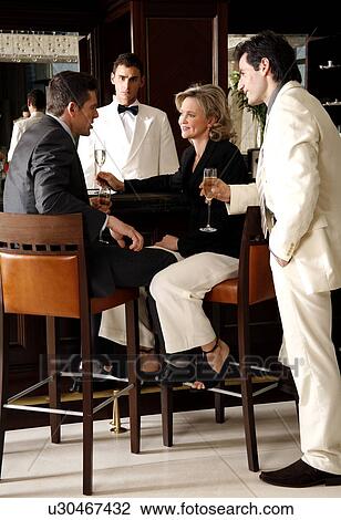 Stock Image - Two men and a woman sitting at a bar drinking. Fotosearch