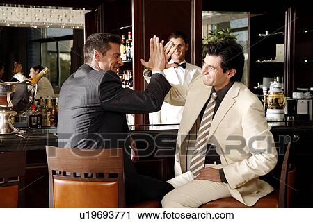 Stock Image - Two men slapping hands in agreement at a bar. Fotosearch