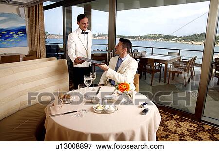 Waiter handing a man the menu in a restaurant View Large Photo Image Stock Photo - Waiter handing a man the menu in a restaurant. Fotosearch