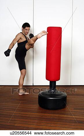 Picture - Young man kicking a punching bag. Fotosearch