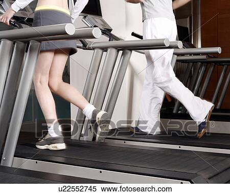 Stock Photography - Young woman and man on treadmill, waste down. Fotosearch
