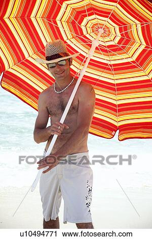 Stock Image - Man on beach with beach umbrella. Fotosearch