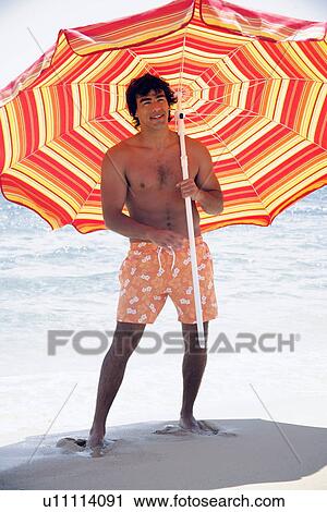 Stock Image - Man on beach with beach umbrella. Fotosearch