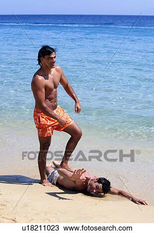 Stock Image - Man stepping on friend on the beach. Fotosearch
