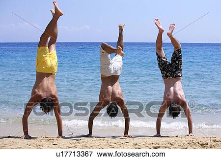 Three young men doing handstands on beach View Large Photo Image Stock Photo - Three young men doing handstands on beach. Fotosearch