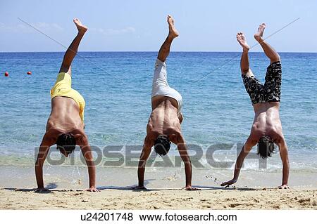 Stock Photo - Three young men doing handstands on beach. Fotosearch