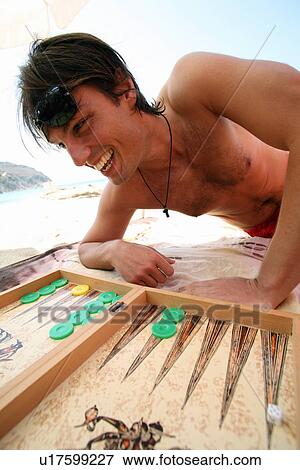 Stock Photo - Young man on beach playing backgammon. Fotosearch
