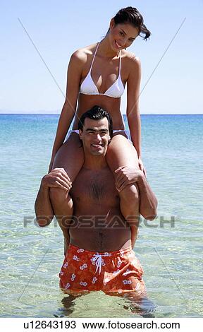 Stock Image - Young woman sitting on man's shoulders. Fotosearch