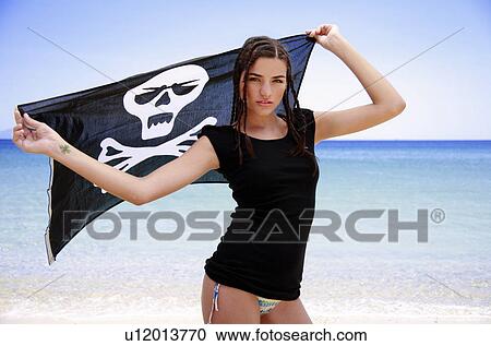 Stock Image - Young woman on beach holding up skull and bones flag. Fotosearch