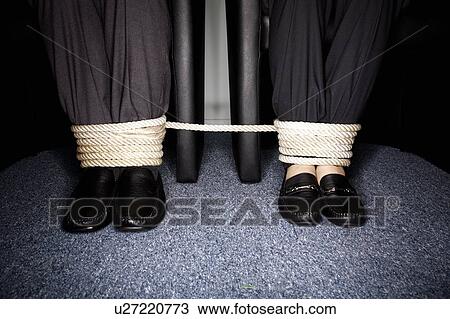 Stock Image - Male and female business people's legs tied. Fotosearch