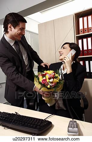 Male office worker giving flowers to female colleague View Large Photo Image Stock Image - Male office worker giving flowers to female colleague. Fotosearch