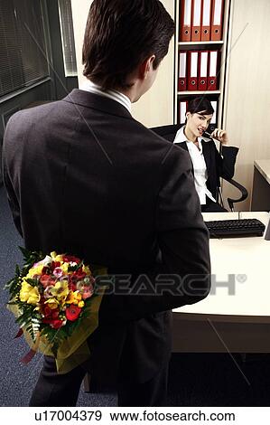 Male office worker hiding flowers for female colleague View Large Photo Image Stock Photo - Male office worker hiding flowers for female colleague. Fotosearch