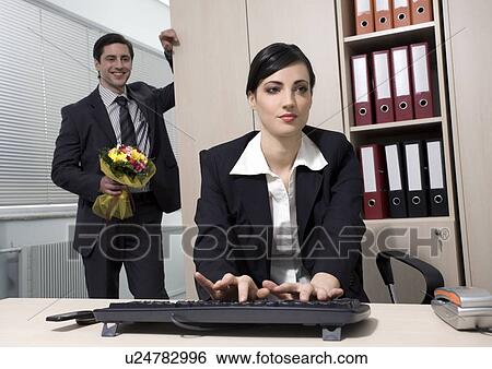 Male office worker hiding flowers for female colleague View Large Photo Image Stock Photograph - Male office worker hiding flowers for female colleague. Fotosearch