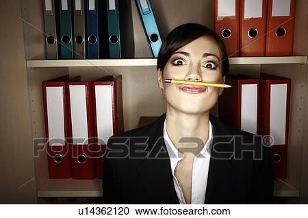 Stock Image - Office worker holding pencil with her upper lip. Fotosearch