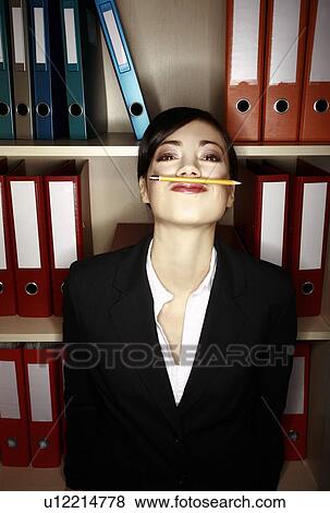 Stock Photo - Office worker holding pencil with her upper lip. Fotosearch