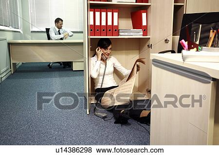 Stock Photo - Office worker on the phone hiding from manager. Fotosearch