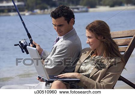 Stock Image - Business couple on beach with fishing rod and laptop. Fotosearch