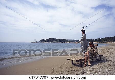 Stock Photo - Business couple on beach with fishing rod and laptop. Fotosearch