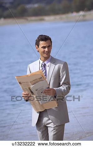 Stock Image - Businessman on beach holding a newspaper. Fotosearch