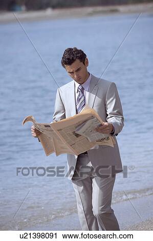 Stock Image - Businessman on beach reading a newspaper. Fotosearch