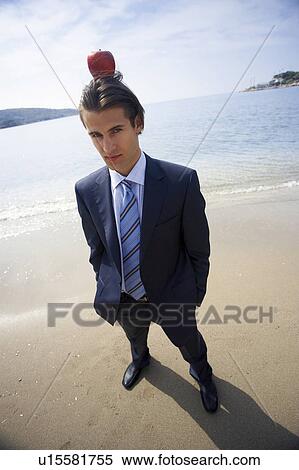 Stock Photography - Businessman on beach with apple balanced on his head. Fotosearch