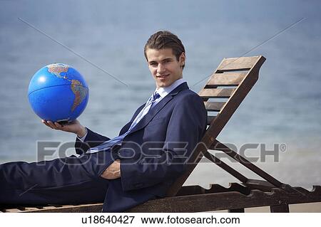 Stock Photo - Businessman on chaise lounge with globe. Fotosearch