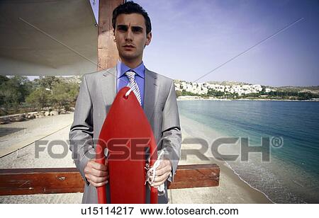 Stock Photo - Businessman on life guard stand with life preserver. Fotosearch