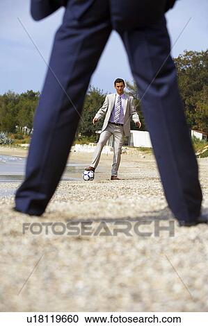 Stock Image - Businessmen on beach playing soccer. Fotosearch